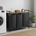 Laundry room with a black 3 section laundry sorter and wooden top, washing machine on the left.