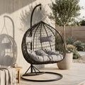Black rattan double hanging chair with grey cushions in an outdoor patio setting