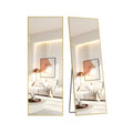 Pale-gold aluminium-framed full-length mirror shown from front and angled views leaning against a wall, reflecting a minimalist living room.