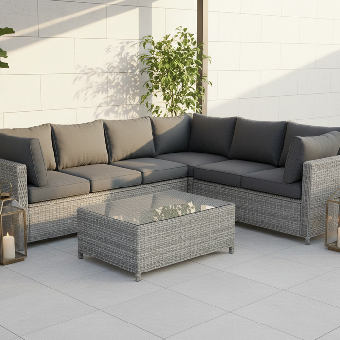 Grey PE rattan corner sofa set with cushions and glass coffee table on a light grey porcelain patio with potted plants