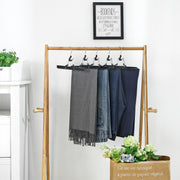 Black skirt hangers holding trousers and a scarf on a wooden clothes rail