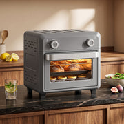 Grey air fryer oven on a dark worktop with lemons and a glass of water