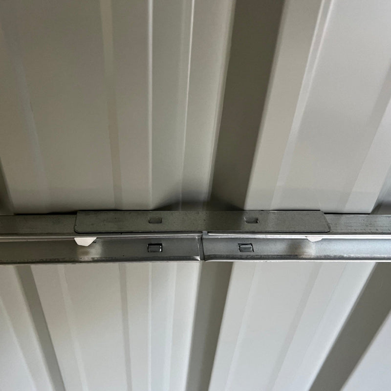 Close-up inside the shed of the pale roof lining and the bolted galvanised steel roof beam