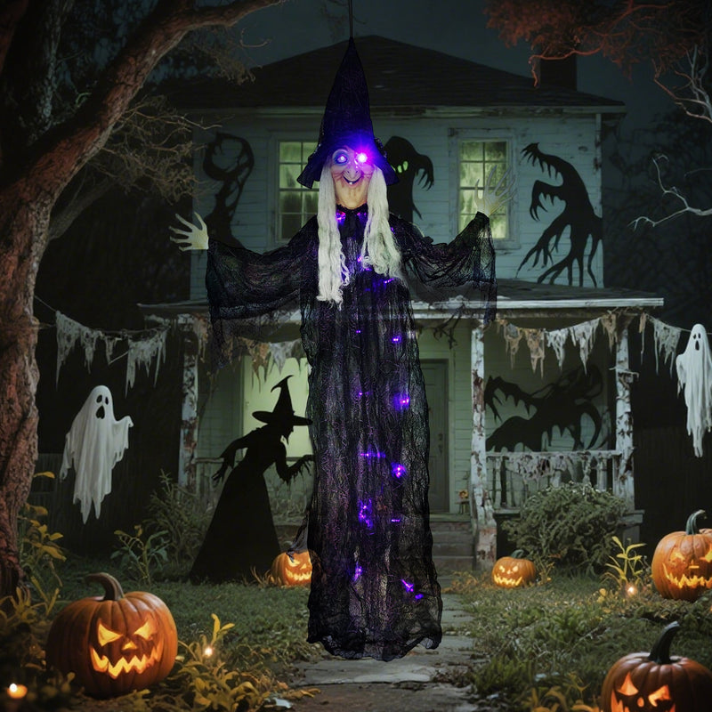 Hanging witch prop displayed in front of a haunted house scene with carved pumpkins