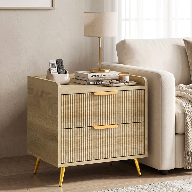 Bedside table beside a sofa arm holding a lamp, books and remote control