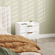 Bedside table next to a bed with a mustard quilted throw and reading glasses