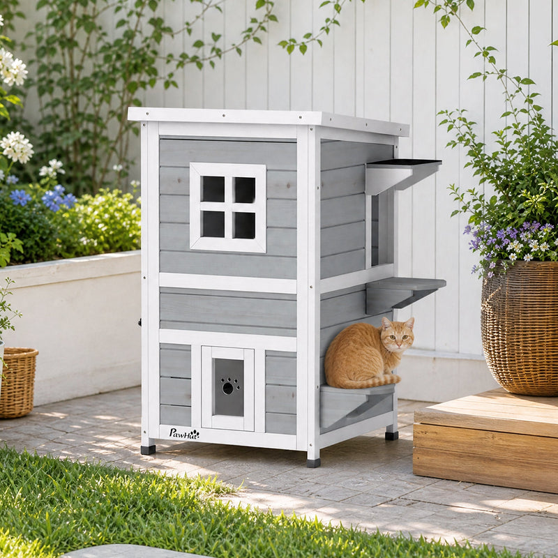 Cat sitting on a jump platform beside the grey 2-floor PawHut cat house on a patio