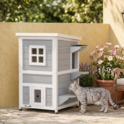 Cat approaching the grey 2-floor PawHut cat house beside potted flowers on a patio