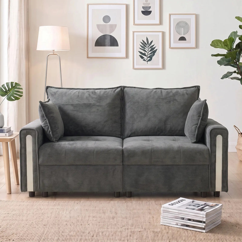 Front view of the loveseat in a living room with framed prints, a floor lamp and a stack of magazines