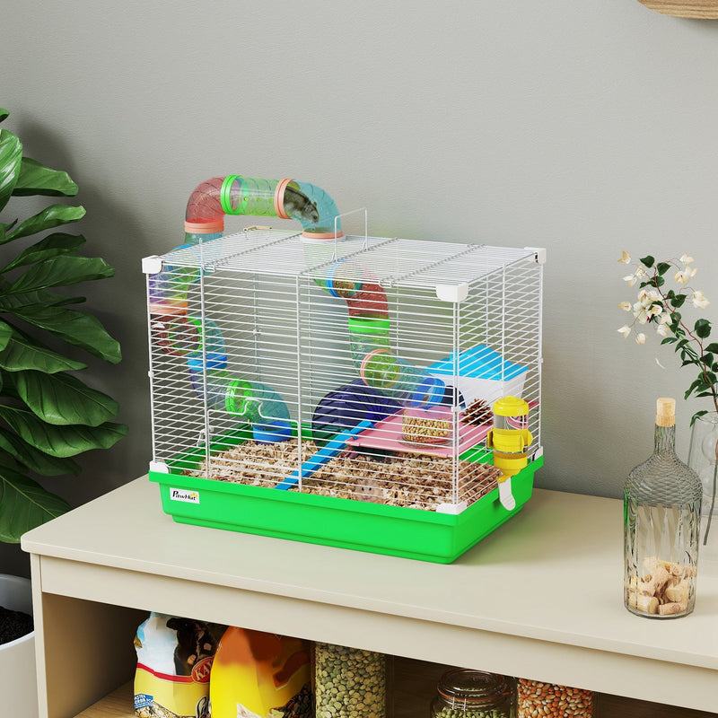 Green PawHut hamster cage with bedding, set on a wooden shelf beside a plant