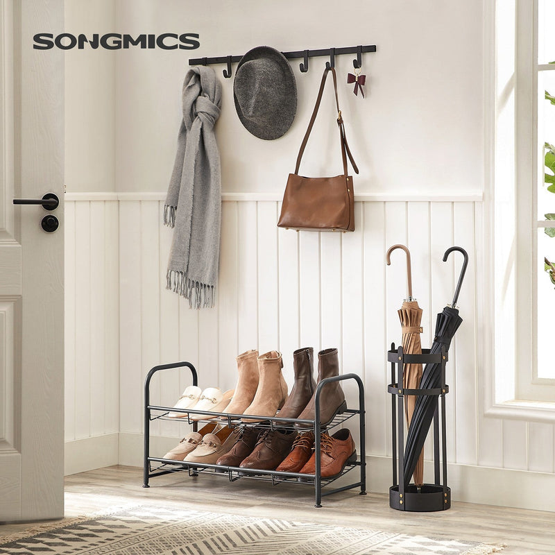 Black 2 tier shoe rack in a hallway under wall hooks, holding boots and shoes