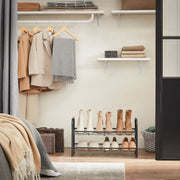 Black 2 tier shoe rack in a wardrobe base holding boots below hanging coats