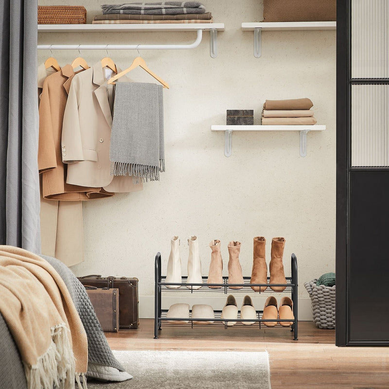 Black 2 tier shoe rack in a wardrobe base holding boots below hanging coats