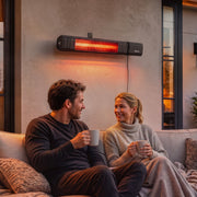 Black wall-mounted patio heater glowing above a couple relaxing on a sofa