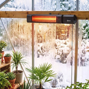Black wall-mounted patio heater fitted in a snowy greenhouse among plants