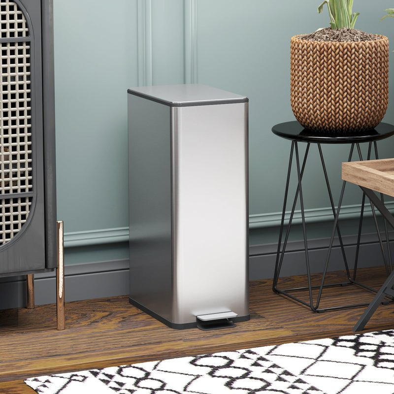 Silver 20L slim stainless steel pedal bin closed in front of a rattan cabinet and side table