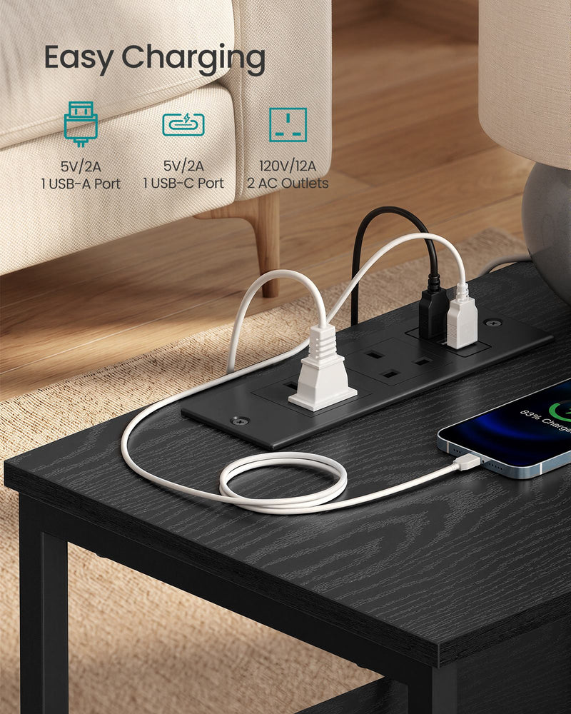 Close-up of the ink black bedside table's built-in power strip with plugs and a phone connected