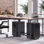 Two black filing cabinets rolled under a shared desk in a brick walled office