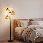 3-light floor lamp glowing beside a bed in a bedroom