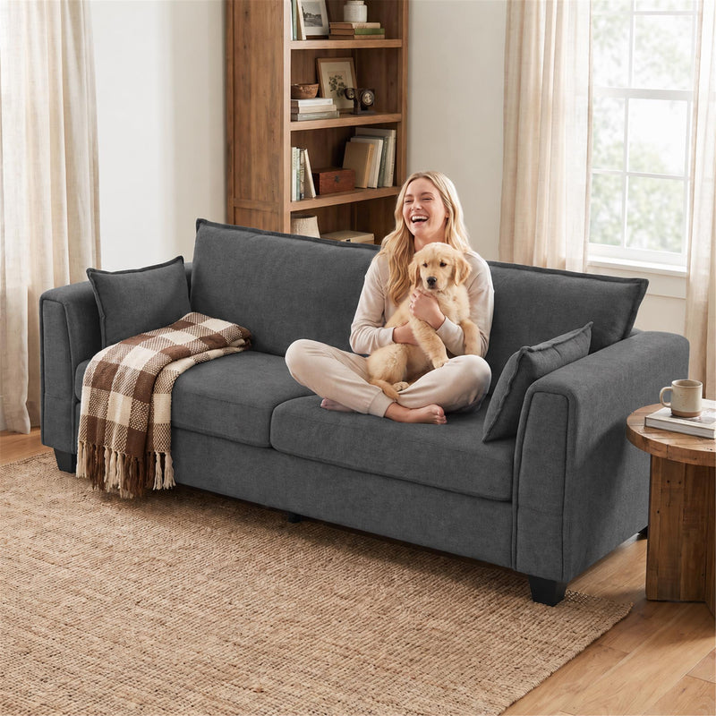 Woman holding a dog on the dark grey sofa next to a bookcase