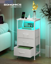 Bedside table beside a bed at night with teal LED lighting and a phone charging on top