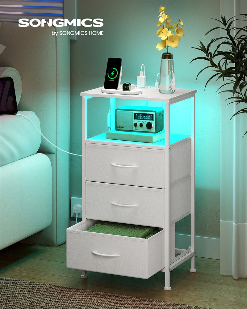 Bedside table beside a bed at night with teal LED lighting and a phone charging on top