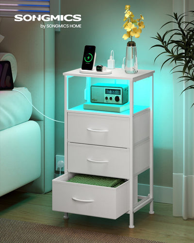 Bedside table beside a bed at night with teal LED lighting and a phone charging on top