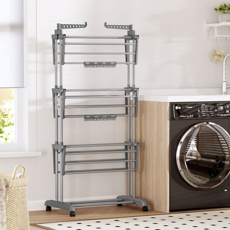 Grey 3-tier clothes airer standing empty next to a black washing machine