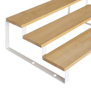 Detail of the bamboo shelves fixed to the white steel frame, showing the three stepped tiers