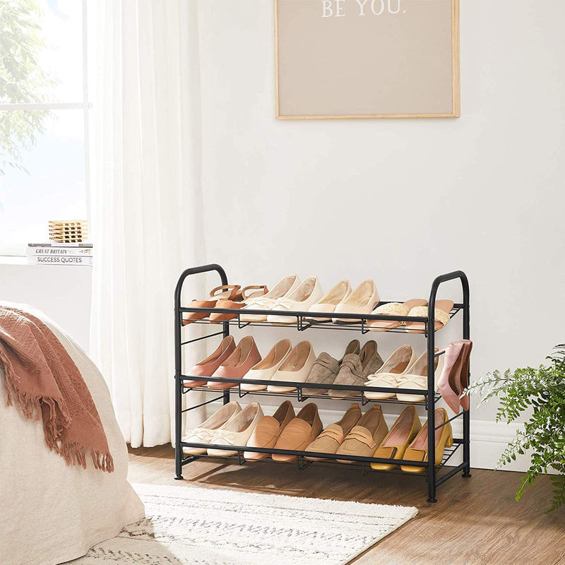 Black 3 tier shoe rack in a bedroom holding three rows of shoes beside a bed