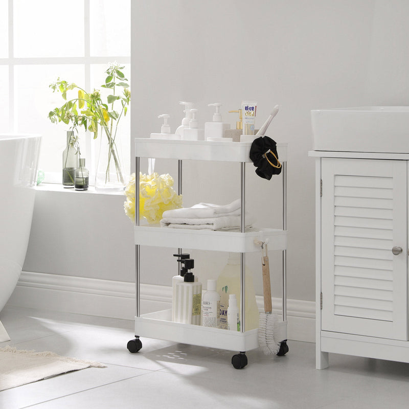 White storage trolley beside a bath holding towels, brushes and pump bottles