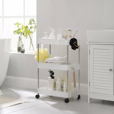 White storage trolley beside a bath holding towels, brushes and pump bottles