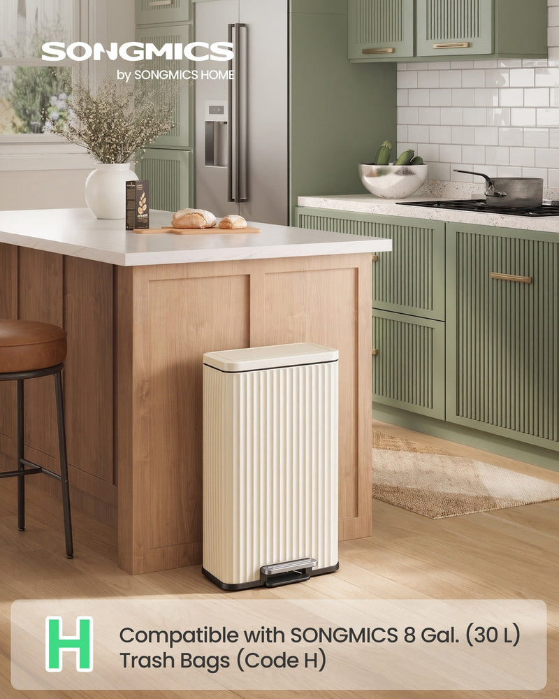 Beige pedal bin beside a wooden kitchen island in a green kitchen