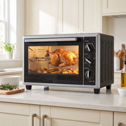 36L mini oven on a kitchen worktop roasting a whole chicken on the rotisserie beside vegetables