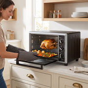 Woman in oven gloves lifting a roasting tray of vegetables from the open mini oven