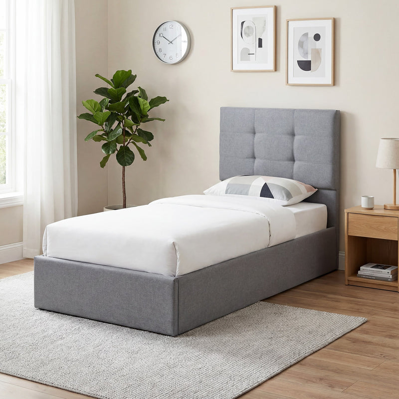 Grey ottoman bed frame styled in a bedroom with a bedside table, clock and pot plant