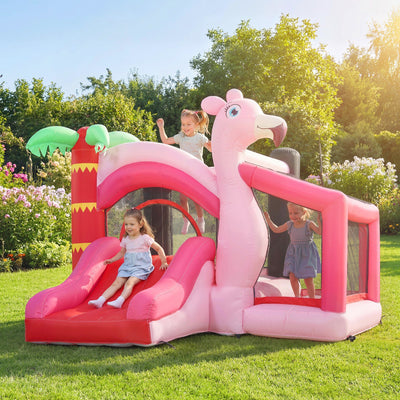 Three children playing on the pink flamingo bounce house in a garden