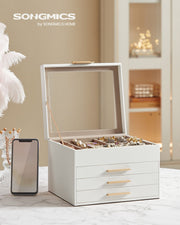Open white jewellery box on a marble table beside a mobile phone showing its size
