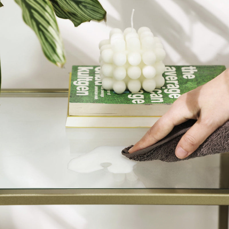 Hand wiping a glass shelf clean with a cloth to show the smooth surface
