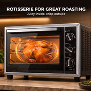 Rotisserie function roasting a whole chicken inside the lit oven
