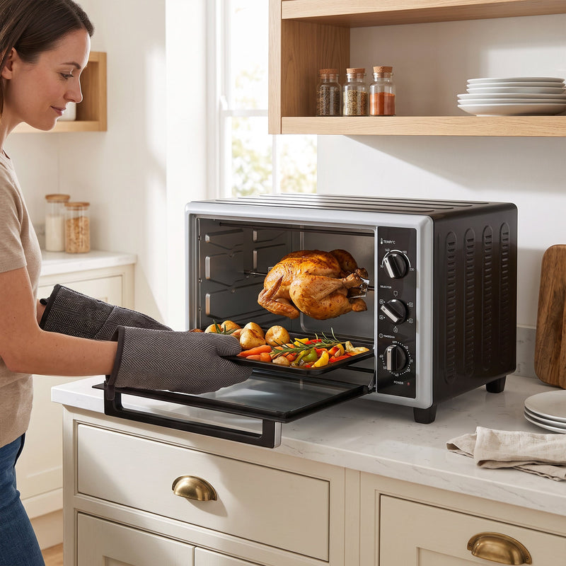 Woman in oven gloves lifting a roasting tray of vegetables from the open mini oven