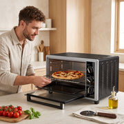 Man sliding a pizza on the wire rack into the open mini oven