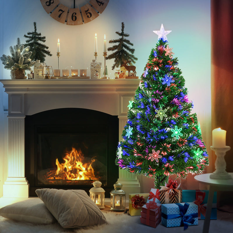 Lit tree beside a fireplace with candles and gifts