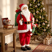 Santa figure with a green sack beside a Christmas tree and music box