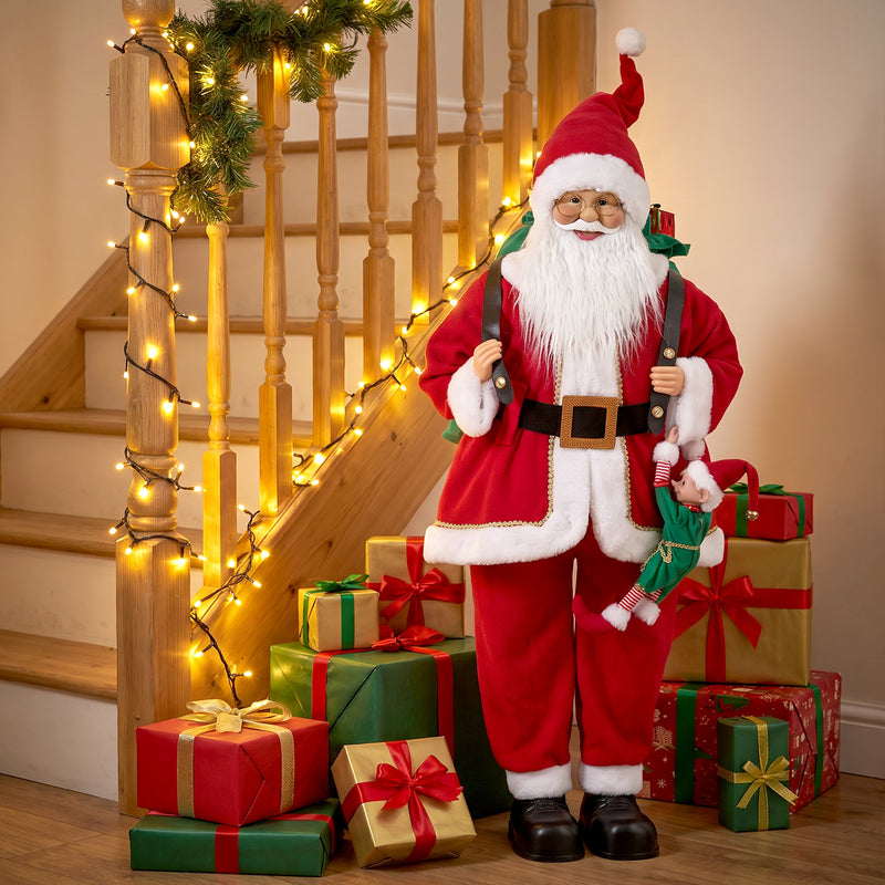Santa figure by a staircase with fairy lights and wrapped gifts