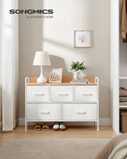 The white and oak chest of drawers in a bedroom with a lamp and framed prints