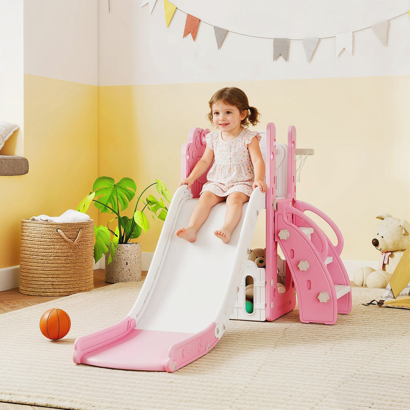Toddler girl sliding down the pink slide in a playroom with bunting decorations