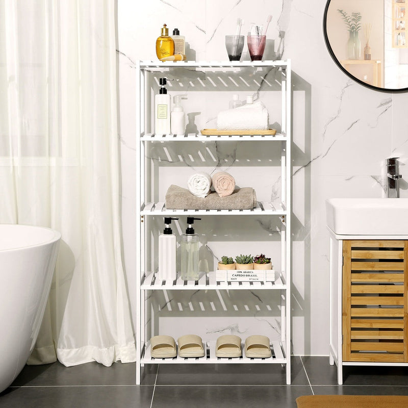 White bamboo shelf next to a bathtub holding folded towels and toiletries
