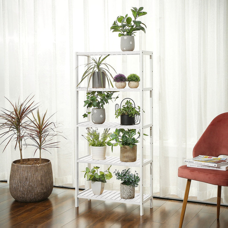 White bamboo shelf displaying potted plants against a curtained window