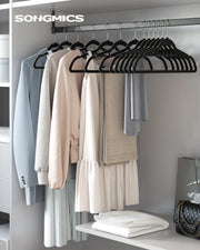 Black velvet hangers holding shirts, trousers and a dress on a wardrobe rail